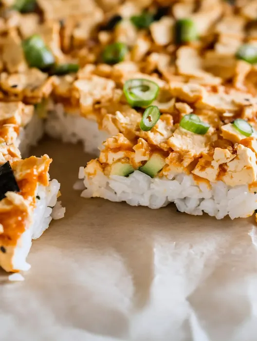 A piece of sushi with vegetables on top.