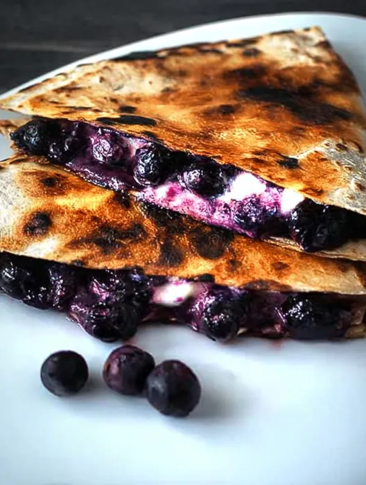 A burnt blueberry pancake with blueberries on top.