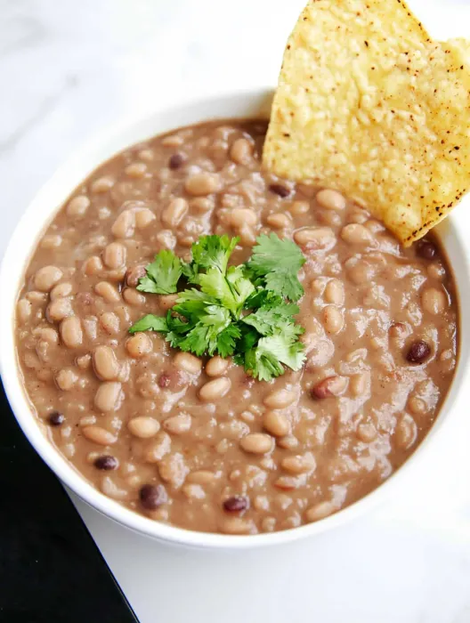 A bowl of beans with a tortilla chip on top.