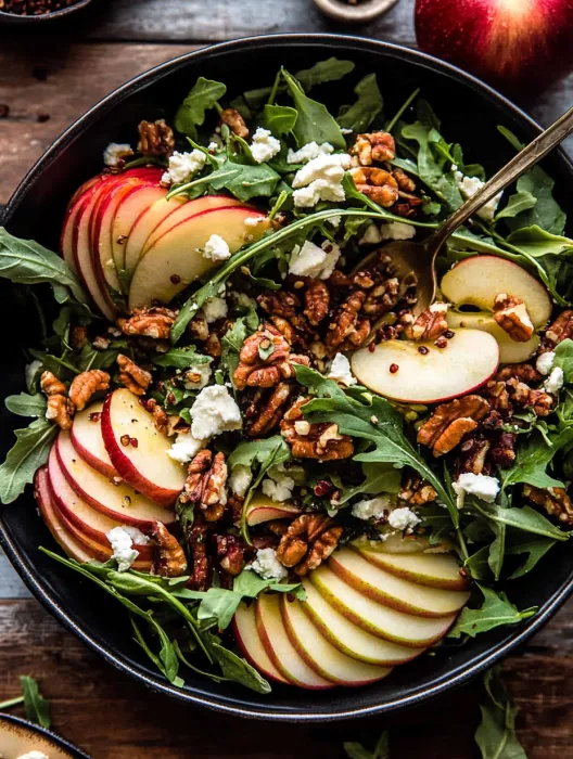 A bowl of salad with apples and walnuts.