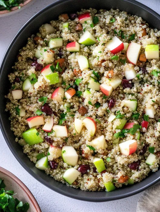 A bowl of food with apples, cranberries, and quinoa.