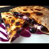 A slice of pizza with blueberries on it.