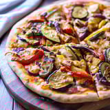 A pizza with various toppings including peppers, mushrooms, and zucchini.