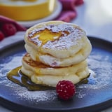 A stack of pancakes with powdered sugar and a raspberry on top.