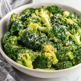 A bowl of broccoli with cheese on top.