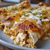 A plate of chicken enchiladas with white sauce.