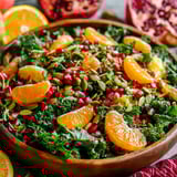 A bowl of salad with oranges, pomegranates, kale, and a honey-lemon vinaigrette.