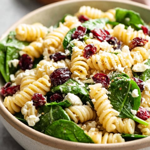 A bowl of pasta salad with spinach, feta, and cranberries.