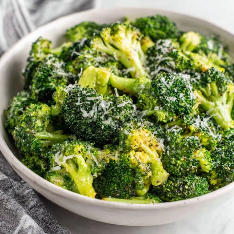 A bowl of broccoli with cheese on top.
