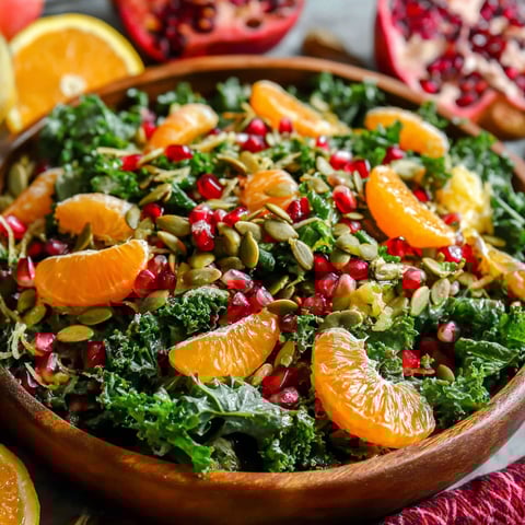 A bowl of salad with oranges, pomegranates, kale, and a honey-lemon vinaigrette.